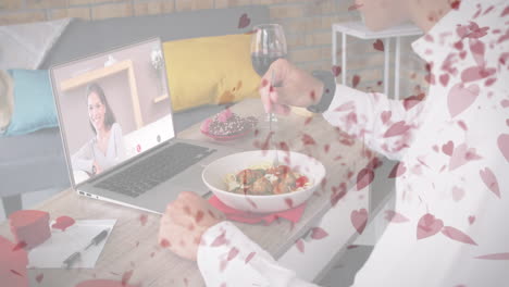여러 개의 빨간 심장 아이콘이 노트북에서 비디오 통화를 하는 동안 점심을 먹고 있는 백인 남성에게 떨어지고 있습니다.