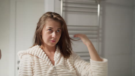 mujer endereza el cabello mojado después de la ducha en el baño ligero. mujer bonita se encuentra cerca del espejo mirando el cabello después de usar cosméticos cuidadosa cámara lenta