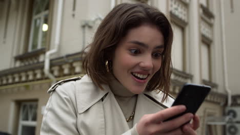 Excited-woman-reading-message-on-phone-outdoor.-Girl-holding-cellphone-in-city.