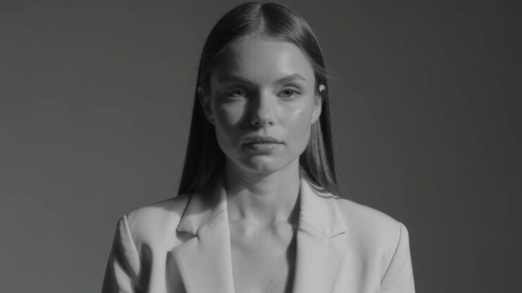 Modella che posa per un ritratto in studio, con blazer chiaro e top scollato, che dischiude le labbra e poi si ricompone.