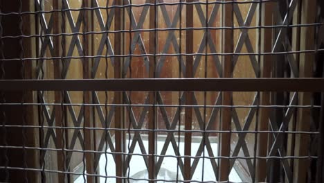 Detailed-tracking-shot-of-the-metal-grid-protection,-wooden-door-and-old-interior-of-an-antique-elevator