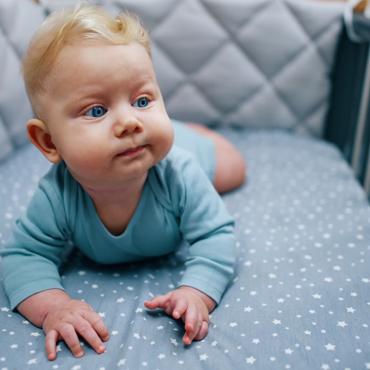 Søt babygutt ligger i vuggen sin. Blåøyd blondt barn ser seg rundt. Nærbilde.