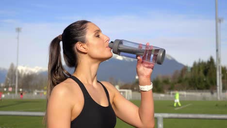 Atractiva-Mujer-Atlética-Bebe-Agua-Después-De-Correr-Tiro-Medio