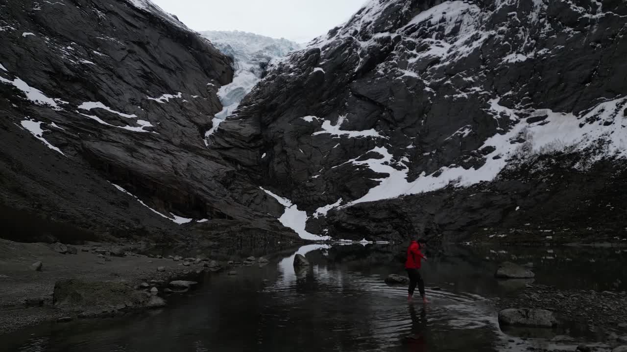 Drone view of A female tourist crossing the lake water at Briksdalsbreen glacier in Norway at winter