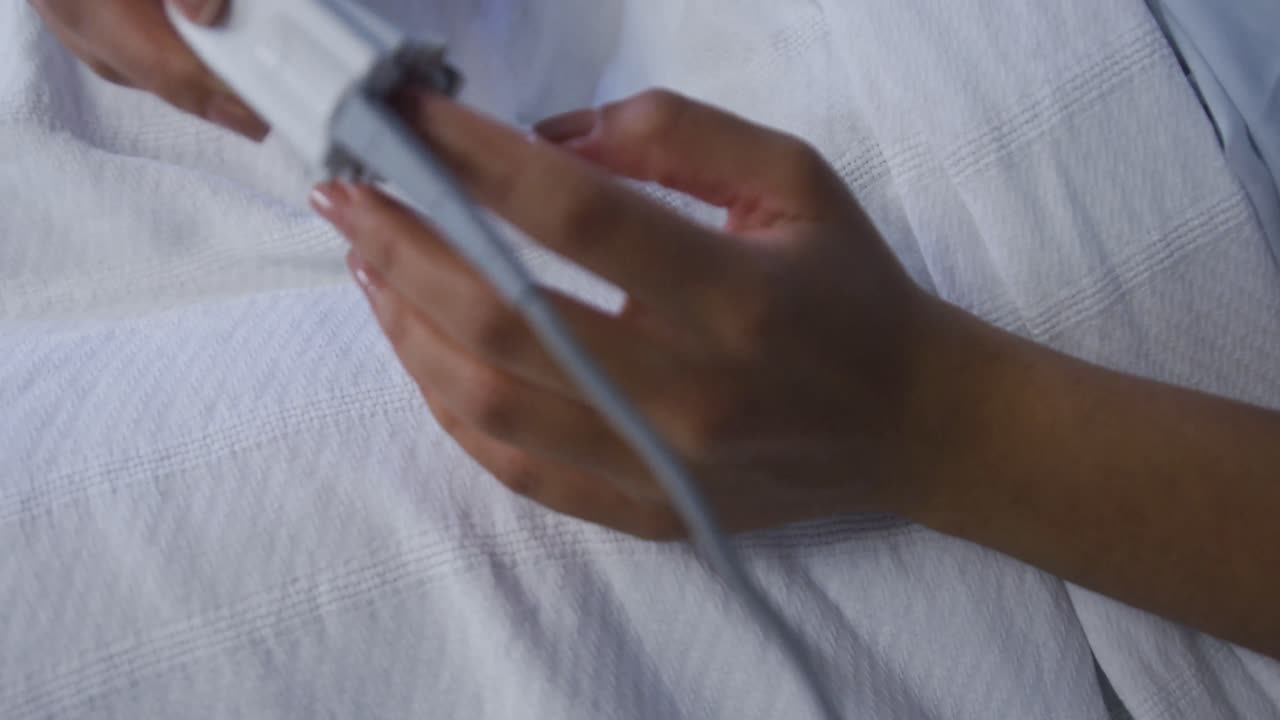 paciente de raza mixta acostada en la cama con un oxímetro de pulso en la punta del dedo