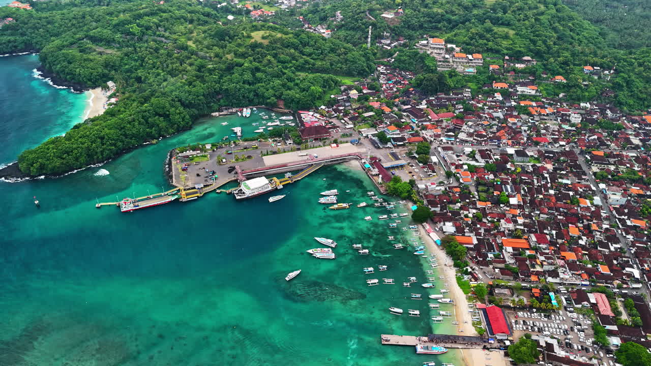 Aerial shot of Padang Bai Beach, showing turquoise waters, harbor, and coastal town in Bali