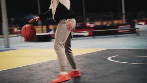 primer plano de una jugadora de baloncesto entrenando y rebotando la pelota en la cancha al aire libre por la noche