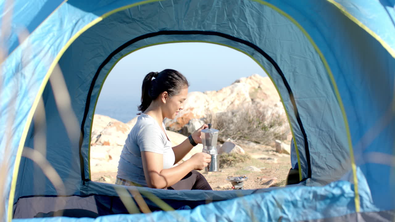 Camping in mountains, woman preparing coffee inside tent, enjoying outdoor adventure
