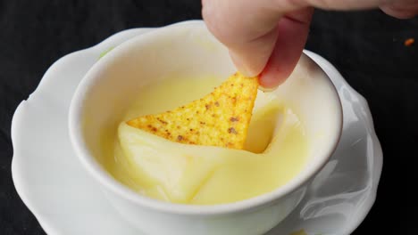 Hand Dipping Crispy Tortilla In Melted Creamy Cheese Sauce In Bowl, Close Up