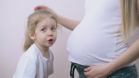 little girl with blue eyes talks to pregnant mommy at home