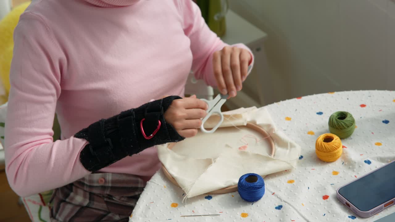 Donna con tutore al polso che ricama un tessuto con fili colorati