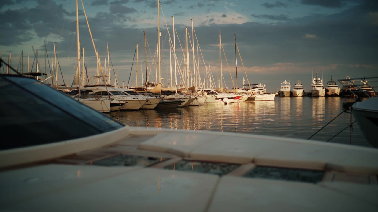 Gros plan d'un pont de yacht de luxe avec une marina légèrement floue et des mâts de voiliers en arrière-plan à Port Vauban, Antibes, sous une lumière de soirée chaleureuse.