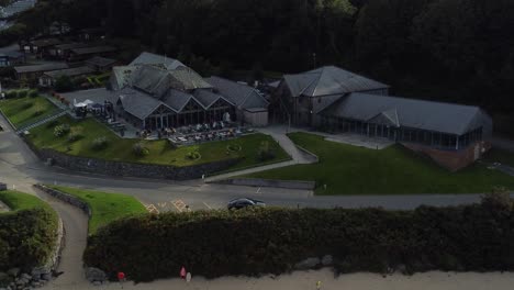 establishing aerial view over old fashioned tavern style beachfront exclusive restaurant shaded by welsh mountainside on secluded beach