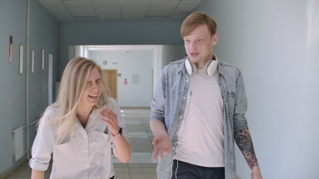 студенты колледжа идут по коридору, смеясь и разговаривая. пара парня и девушки идут в колледж.