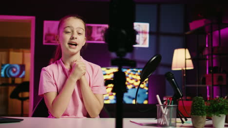 Panning-shot-of-youngster-filming-video-with-phone-on-tripod-in-pink-neon-lit-living-room