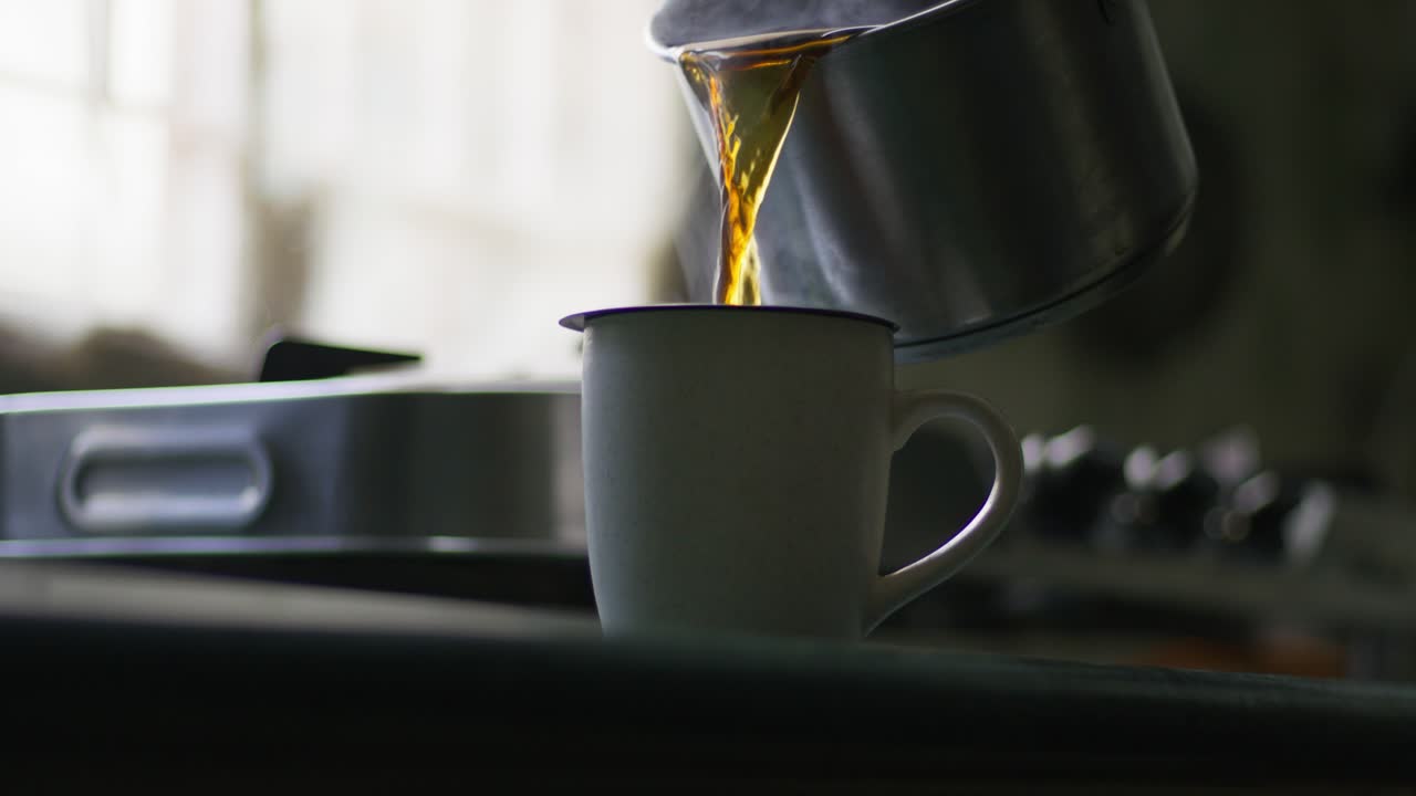 A close-up, slow-motion of pouring tea into a white mug in a kitchen against a blurred background