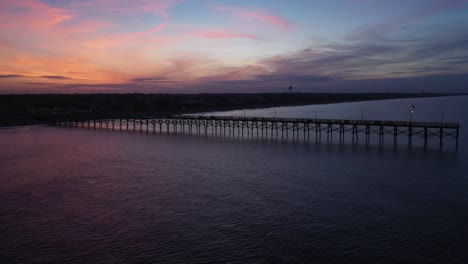 Drohnenaufnahmen-Vom-Sonnenaufgang-Hinter-Einem-Pier,-Während-Sich-Die-Drohne-Aufs-Meer-Hinausbewegt