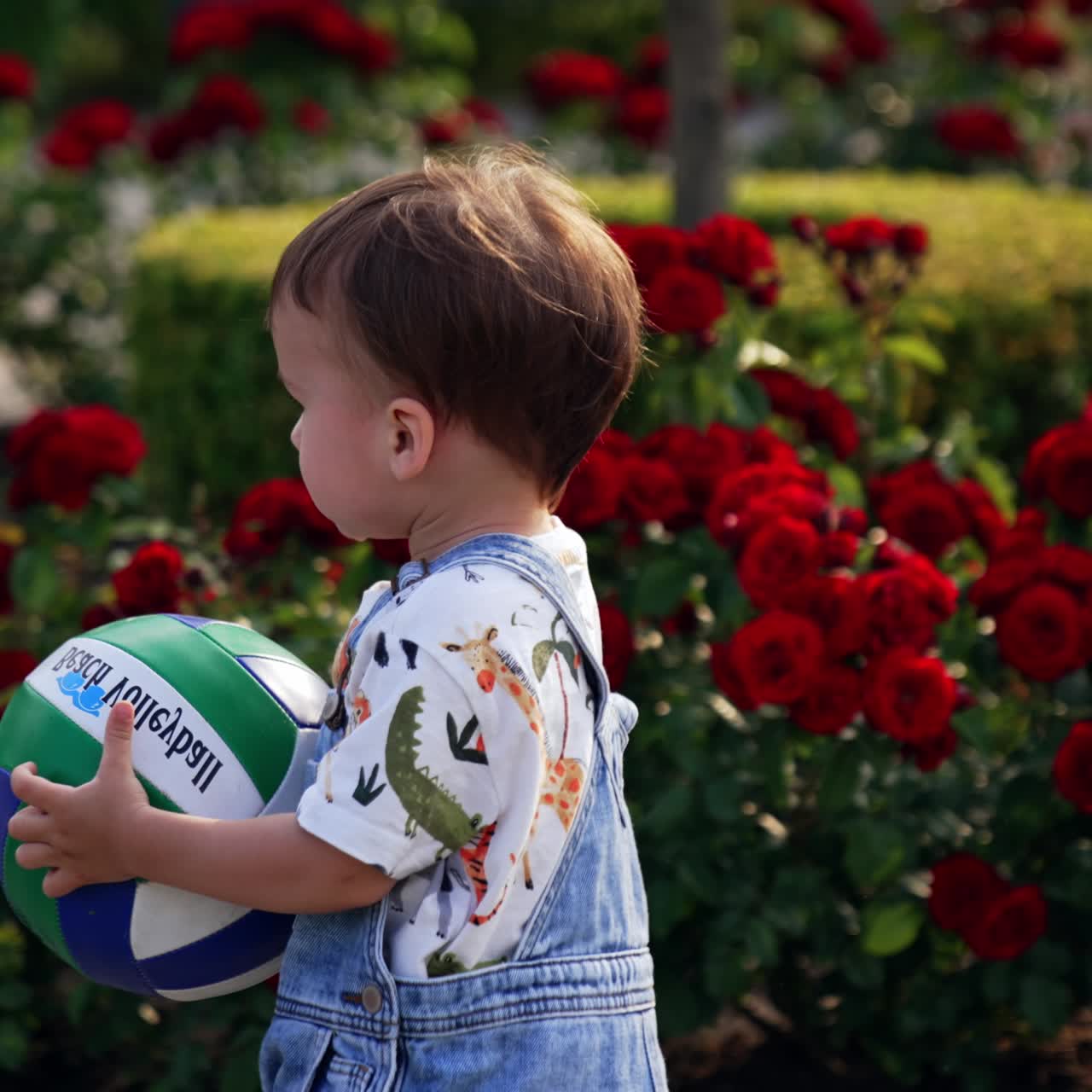 Adorable kid runs with a ball by the park in summer. Baby boy plays outdoors