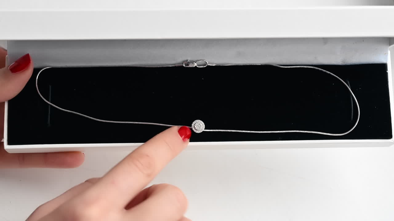 Close view of a woman touching necklace with diamonds. Box, hands with red nails