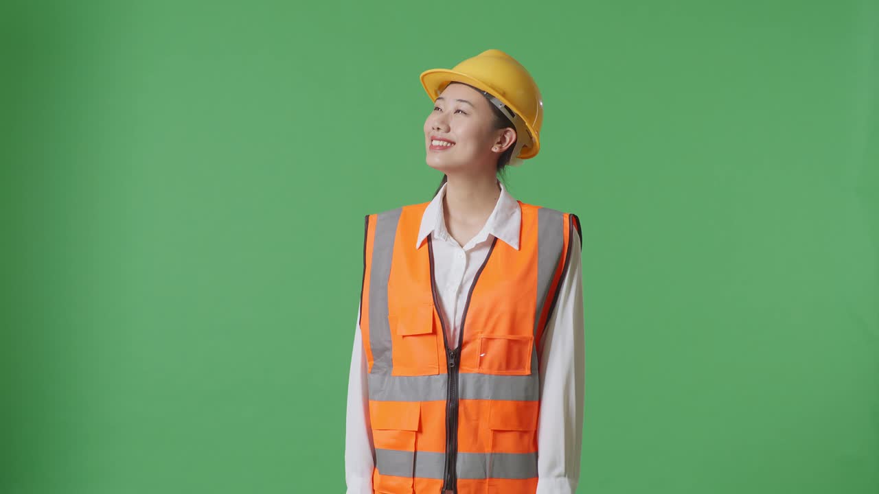 ingeniera asiática con casco de seguridad mirando a su alrededor mientras está de pie en el estudio de fondo de la pantalla verde