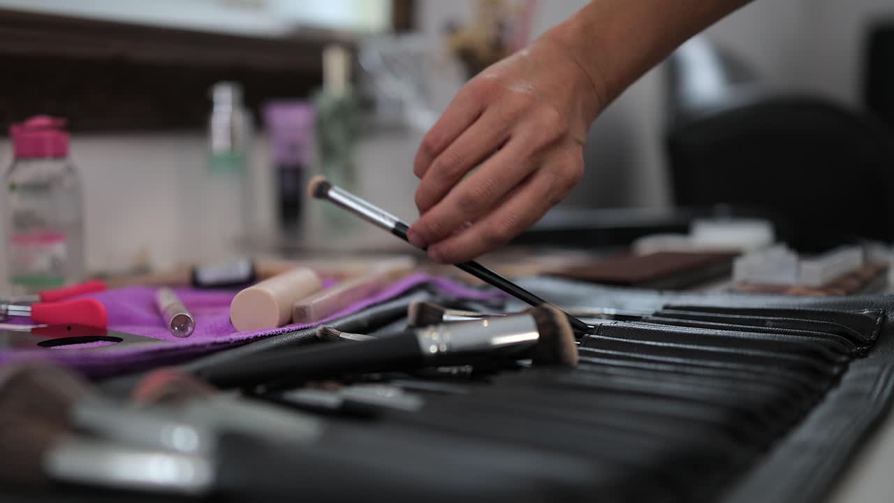 Woman's hand picks makeup brush from aesthetics kit on counter top