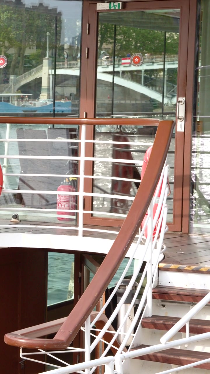 Static shot of a cruise ship deck with stairs, railings, and reflections of Paris architecture