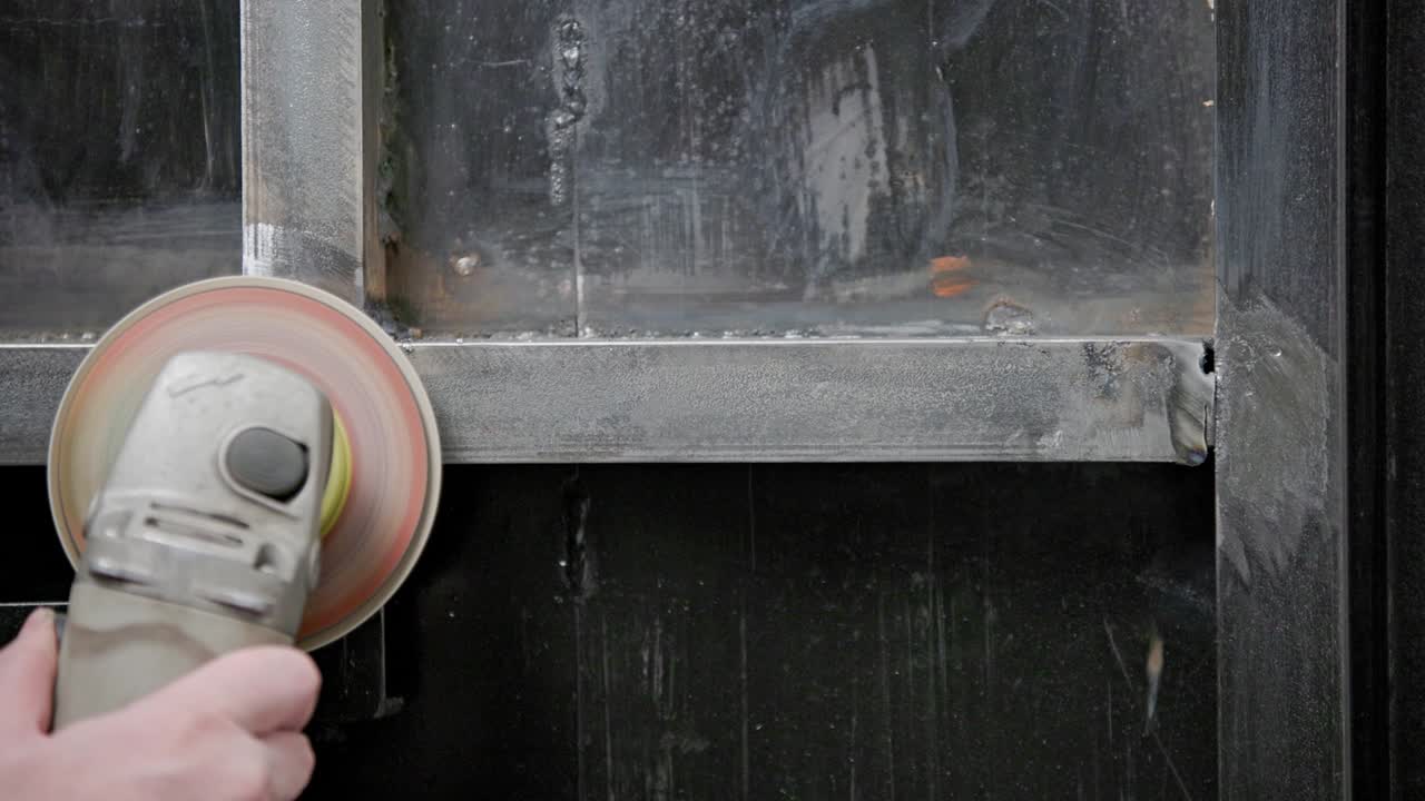 코카시안 손으로 용접 된 접합을 청소하는 글 그린더와 플래프 디스크로 용접 된 금속 구조에 긴 스파크 트레일과 함께 클로즈업, 느린 동작