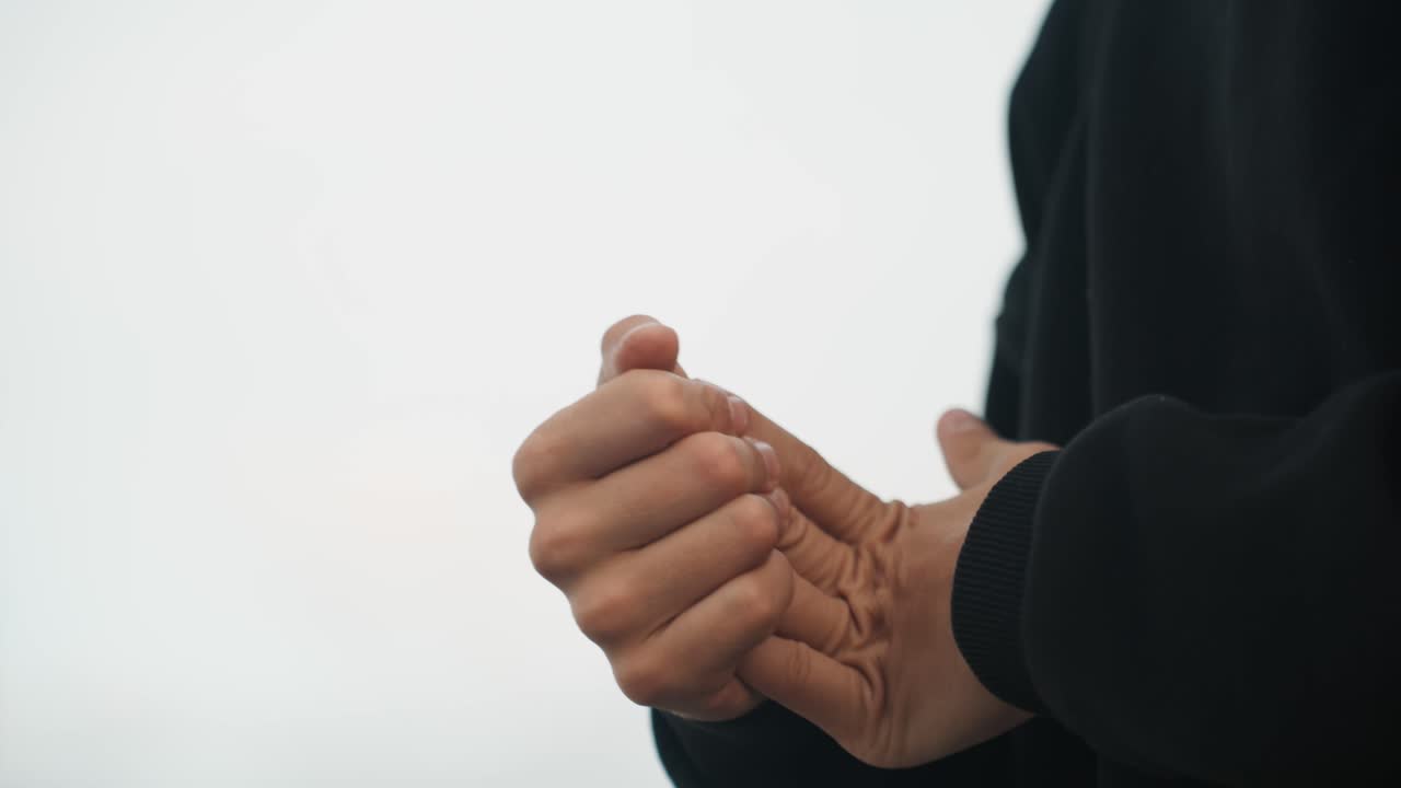 Mani che si scaldano con sfregamenti vigorosi, persona con maglione nero che strofina energicamente i palmi e intreccia le dita, luce fredda esterna, il movimento e la stretta delle nocche suggeriscono mani fredde o pre-esibizione.