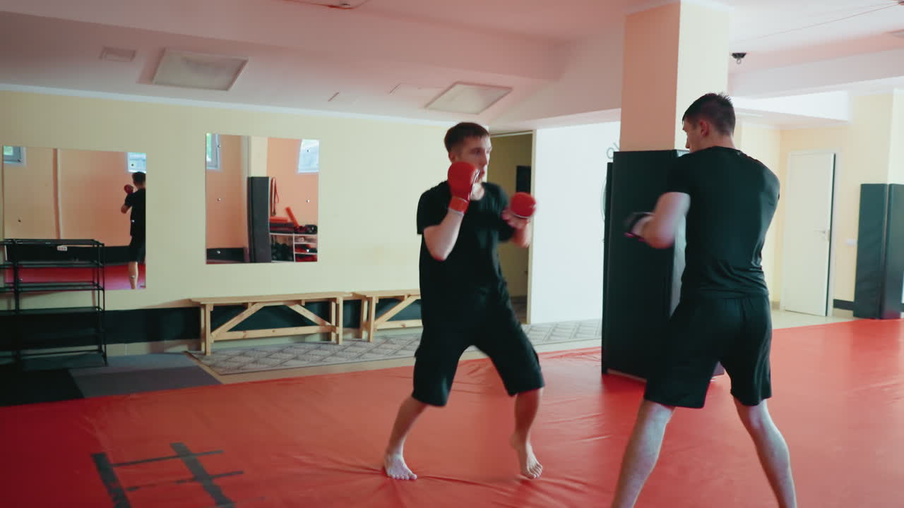 Karate practitioners preparing for sparring session inside dojo with red mats, wearing boxing gloves, focusing on stance and guard, practicing combat training with determination, focus