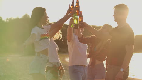 Junge-Leute-Tanzen-Unbeschwert-Am-Sandstrand.-Sie-Verbringen-Fröhlich-Ihre-Zeit-Und-Stoßen-Auf-Der-Open-Air-Party-Am-Flussufer-Mit-Bier-An.