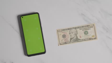 Overhead-Currency-Shot-Of-Hand-Putting-Down-US-10-Dollar-Bill-Next-To-Green-Screen-Mobile-Phone-