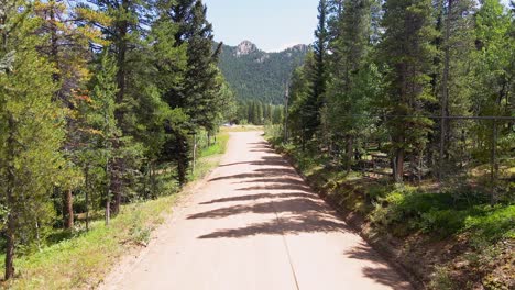 Aerial-dolly-forward-following-a-remote-dirt-road-in-the-mountains-of-Colorado-with-pine-trees-and-grass-travelling-by-the-camera