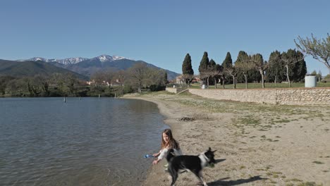 a young child and her black and white dog playing at water edge, aerial