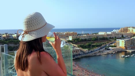 girl drinks a glass of wine over looking a beautiful beach while on holiday in malta