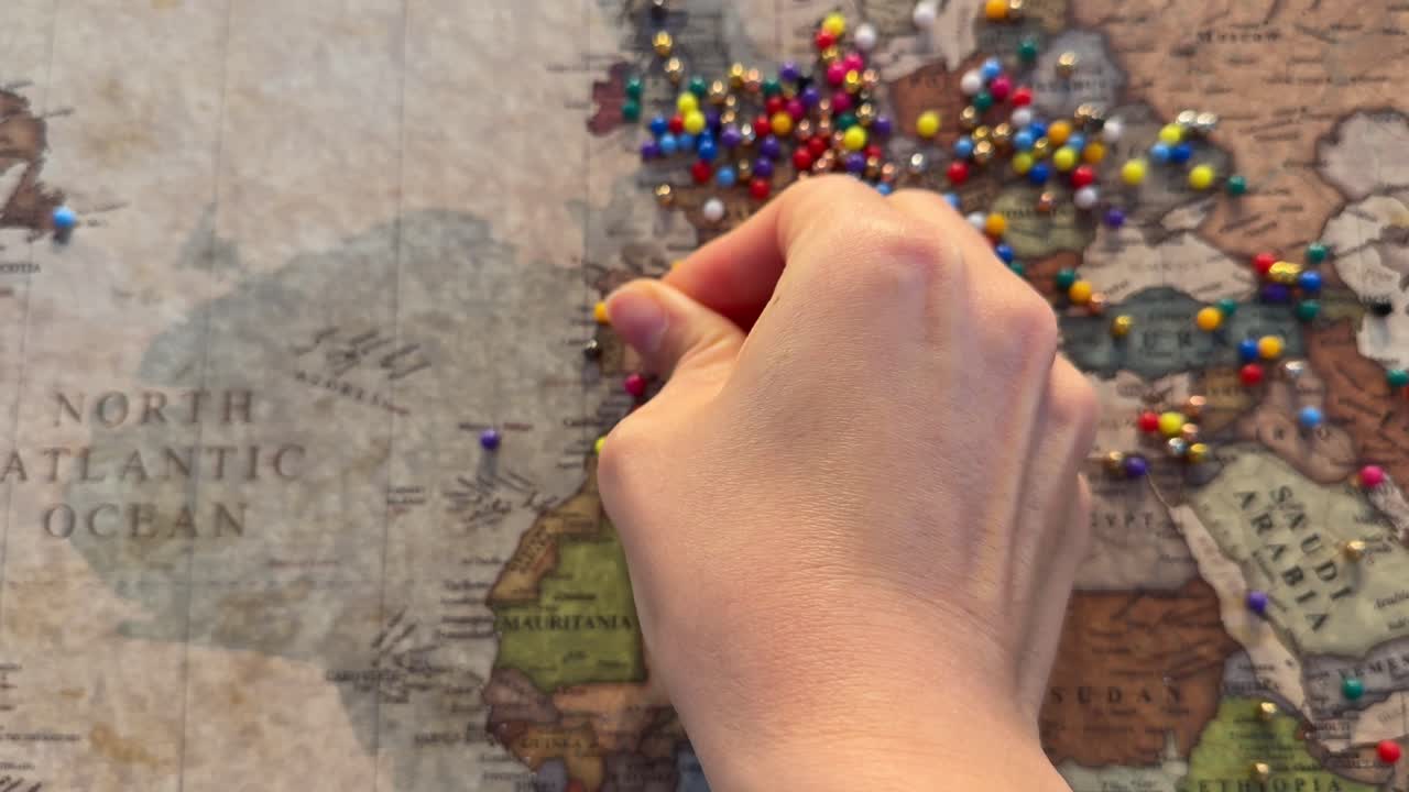Mano che posiziona puntine colorate su una mappa del mondo vintage.