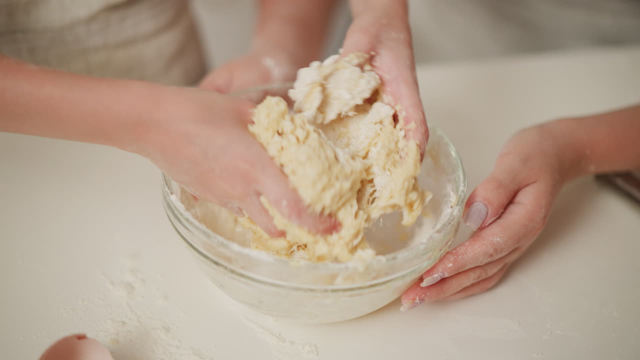 Close up hand view of baker kneading soft dough in glass bowl on floured surface during cooking preparation, fingers pressing mixture as flour sticks to hands while forming smooth consistency