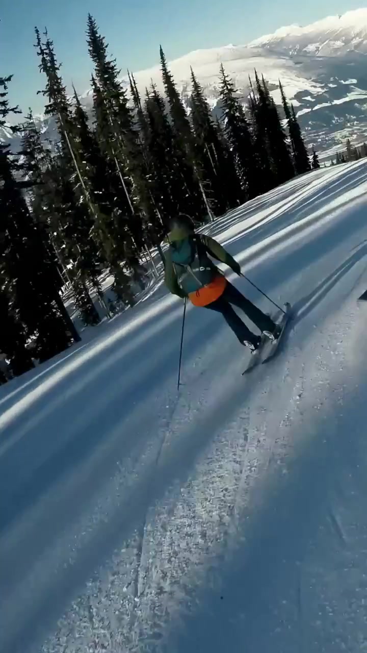 Video verticale: Telecamera che segue uno sciatore con giacca rossa e pantaloni viola mentre gli sciatori scolpiscono le curve, spazio per il testo.