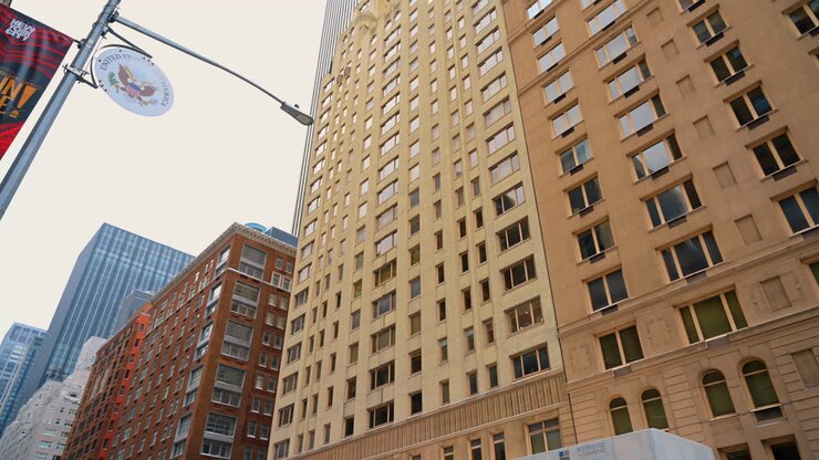 Fachada de arranha-céu em Midtown, Nova York. Edifício bege de calcário com grade densa de janelas e detalhes arqueados que se eleva contra o céu cinzento ao lado de um arranha-céu moderno