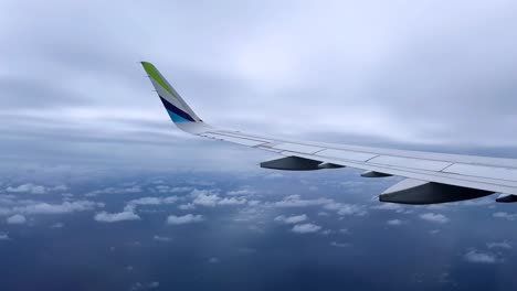 airplane wing view during mid-flight above the clouds with a calm, overcast sky