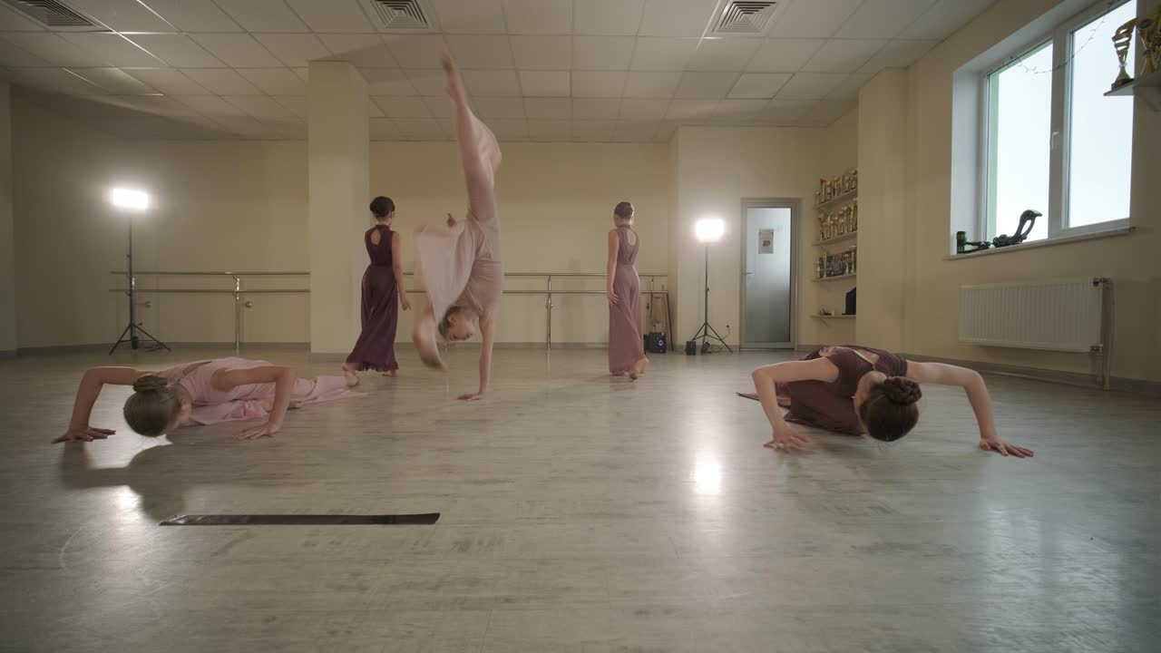 검은색 댄스웨어를 입은 젊은 발레 학생들이 나무 바닥과 벽에 장착된 바를 가진 넓은 발레 스튜디오에서 자세를 연습하는 그룹.