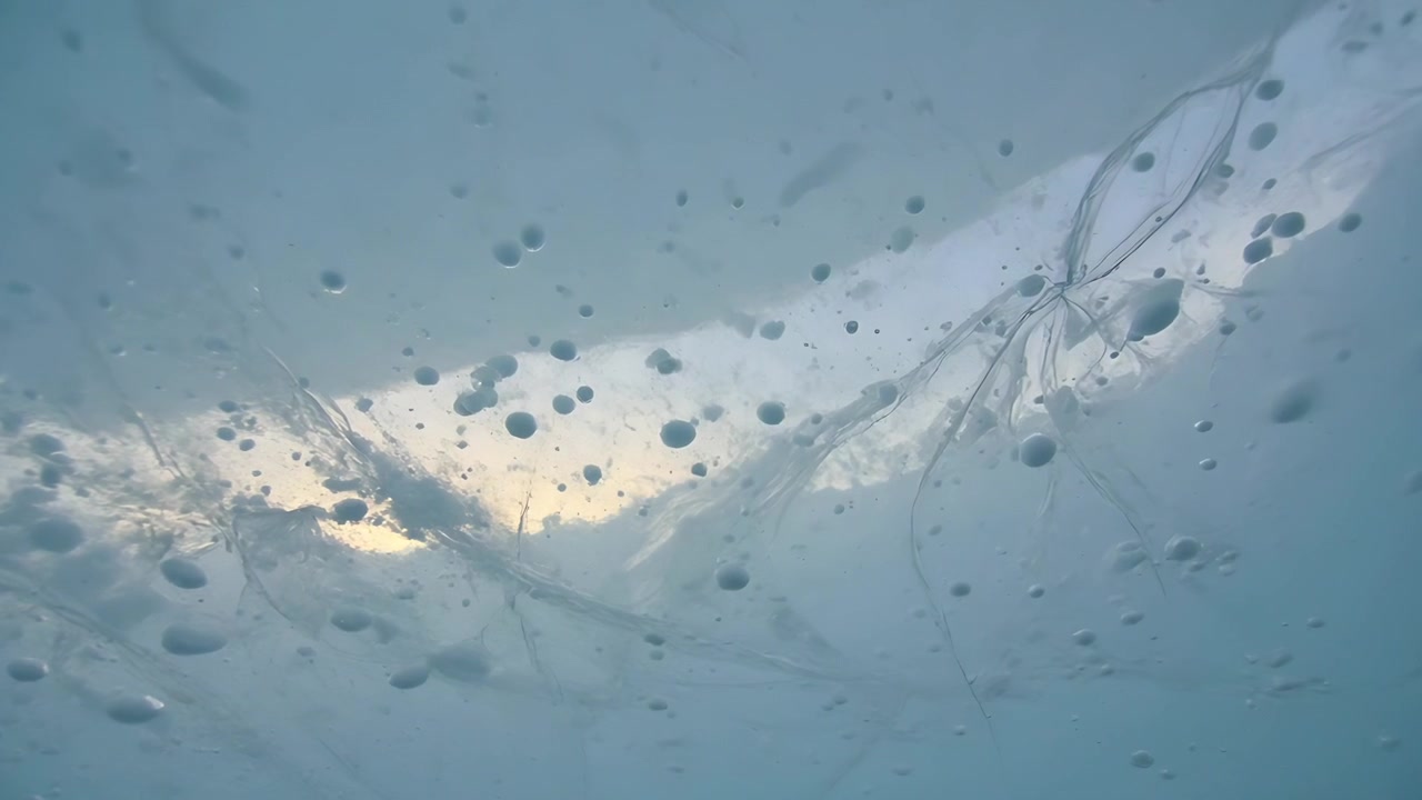Shifting under thin translucent lake ice responding to sun break, fractures and bubbles drifting