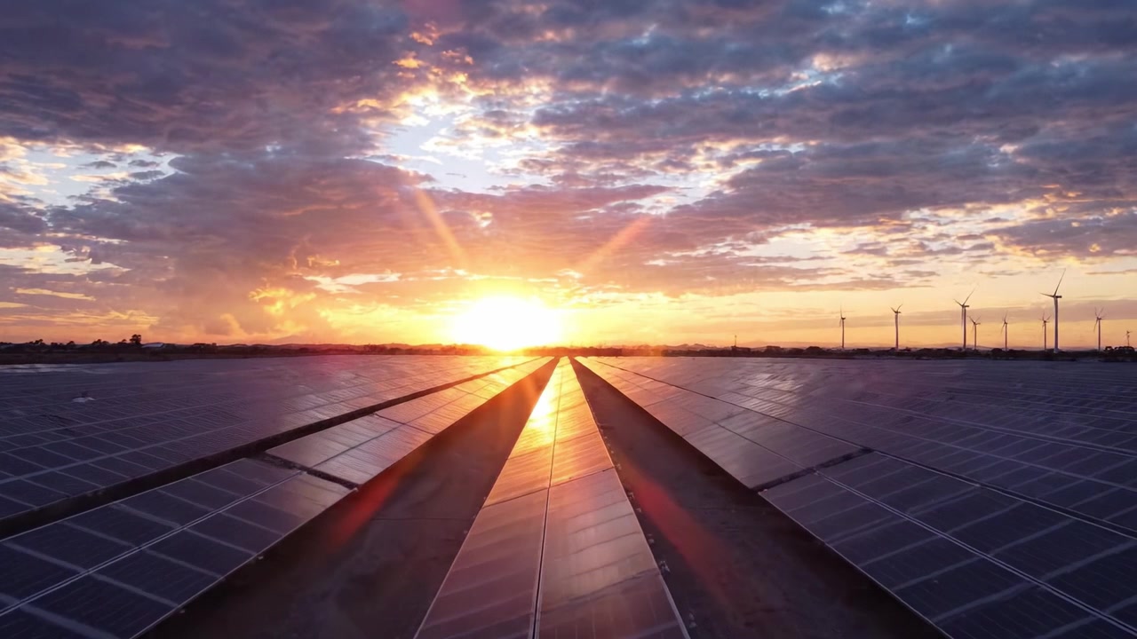 En betagende solnedgang over solpaneler og vindmøller i et ekspansivt landskab med vedvarende energi, der viser harmonien mellem natur og teknologi