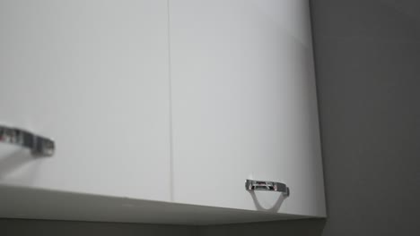 a woman's hand opening a white kitchen cabinet