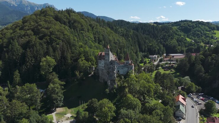 Ripresa aerea orbitale da lontano che mostra il Castello di Bran, immerso in un vasto e rigoglioso paesaggio della Transilvania