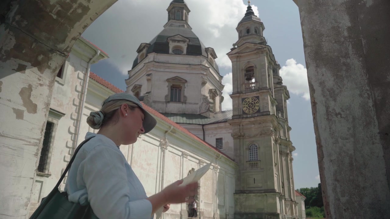 Viaggiatrice solitaria legge una guida cartacea mentre visita lo storico Monastero di Pažaislis in una calda giornata estiva