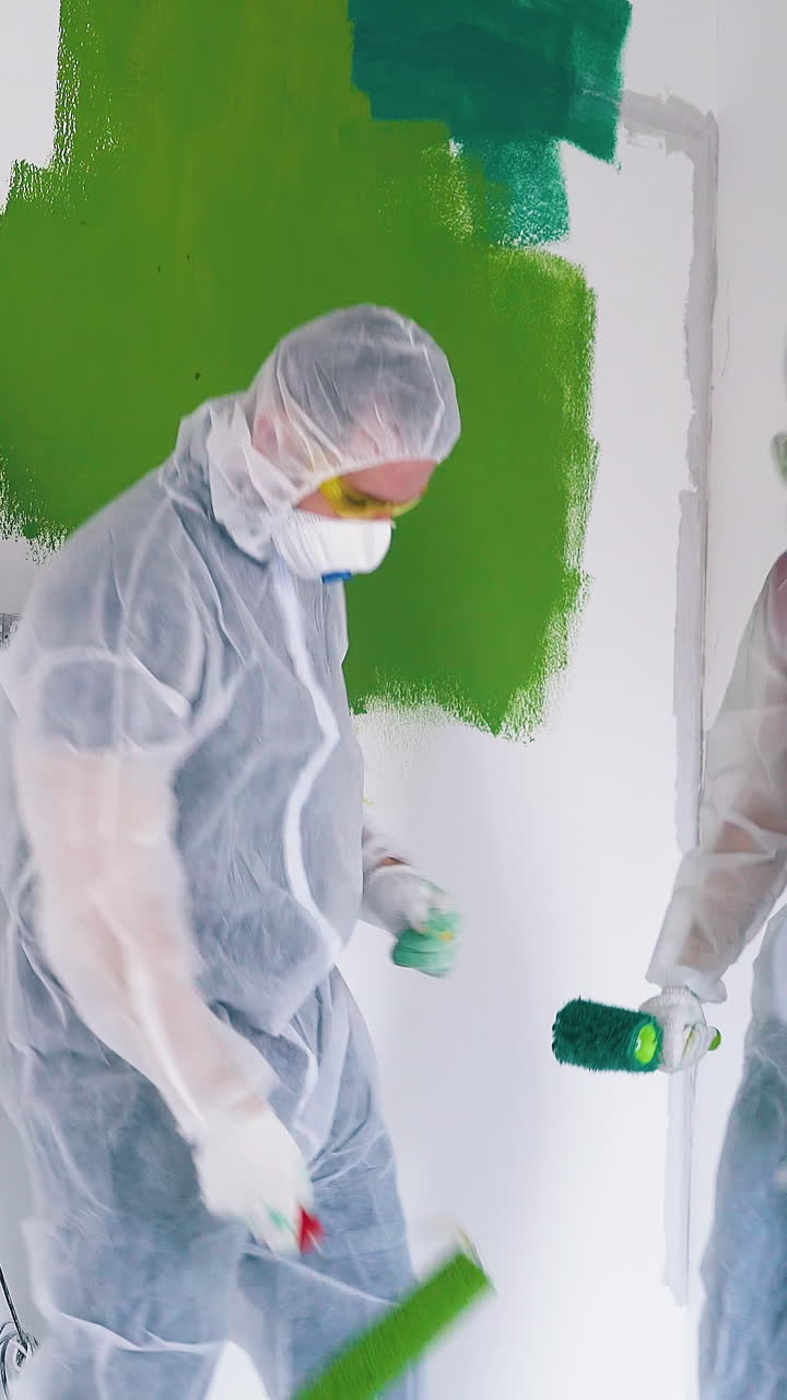 Dolly cam shot: positive family in protective suits and masks dances near white wall with color strokes in light room
