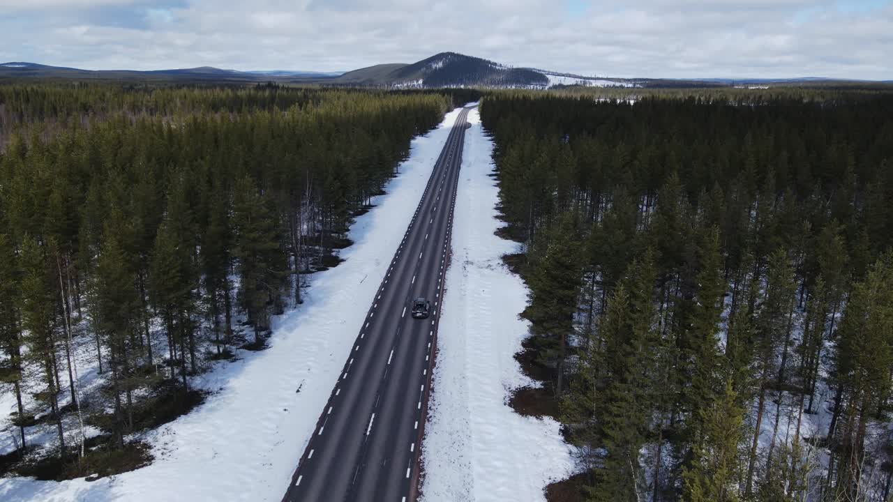스웨덴의 비어있는 고속도로를 가로질러 운전하는 자동차의 공중 추적 은 눈과 바나무로 둘러싸여 있습니다.