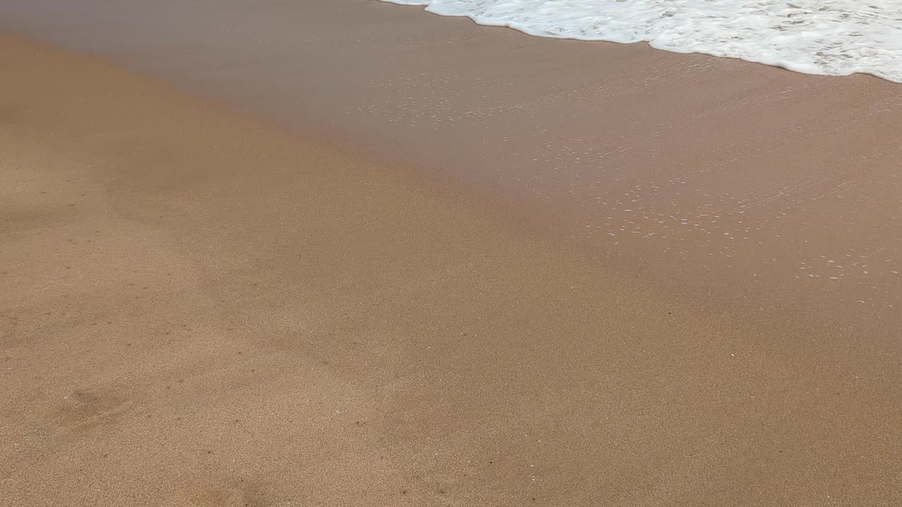 Closeup of frothy whitewash waves rolling up onto sandy beach at tropical island destination
