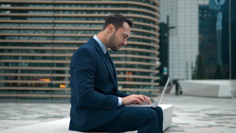 Hombre-De-Negocios-Con-Traje-Escribiendo-En-Una-Computadora-Portátil-Durante-Una-Reunión-Virtual-Fuera-De-Su-Edificio-De-Oficinas-En-Seúl,-Corea-Del-Sur