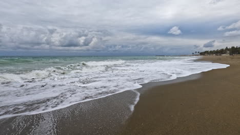 4K-Aufnahme-Eines-Leeren-Braunen-Sandstrandes-Mit-Weißem-Und-Blauem-Wasser-In-Marbella,-Spanien